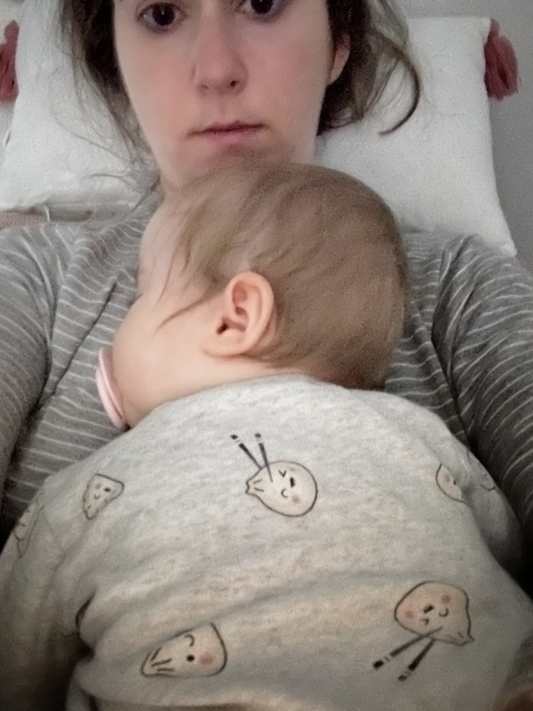 Kylie lying back on a pillow, looking at the camera, with her baby daughter asleep on her chest